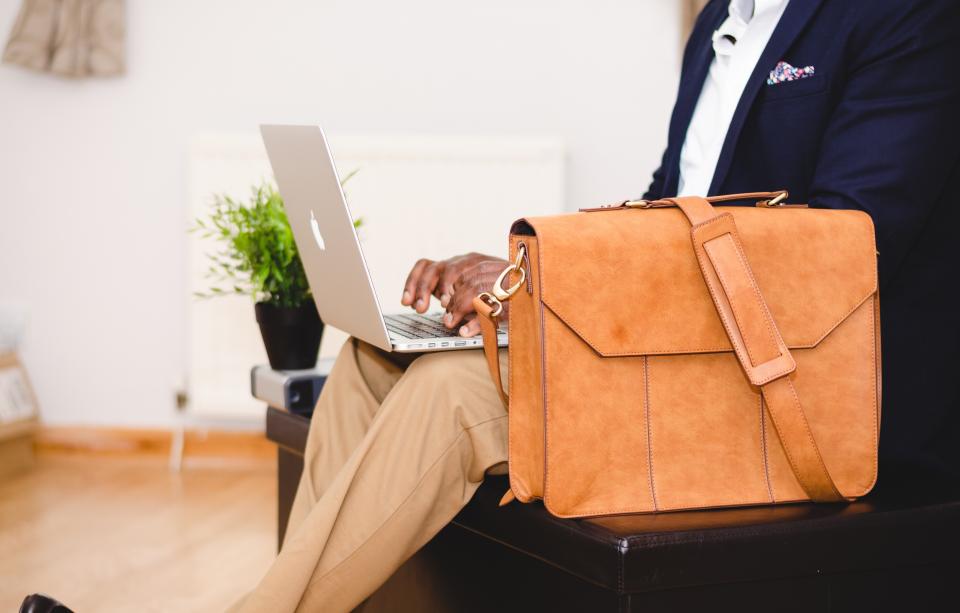 A banker in a navy suit typing on a laptop, leather briefcase beside him